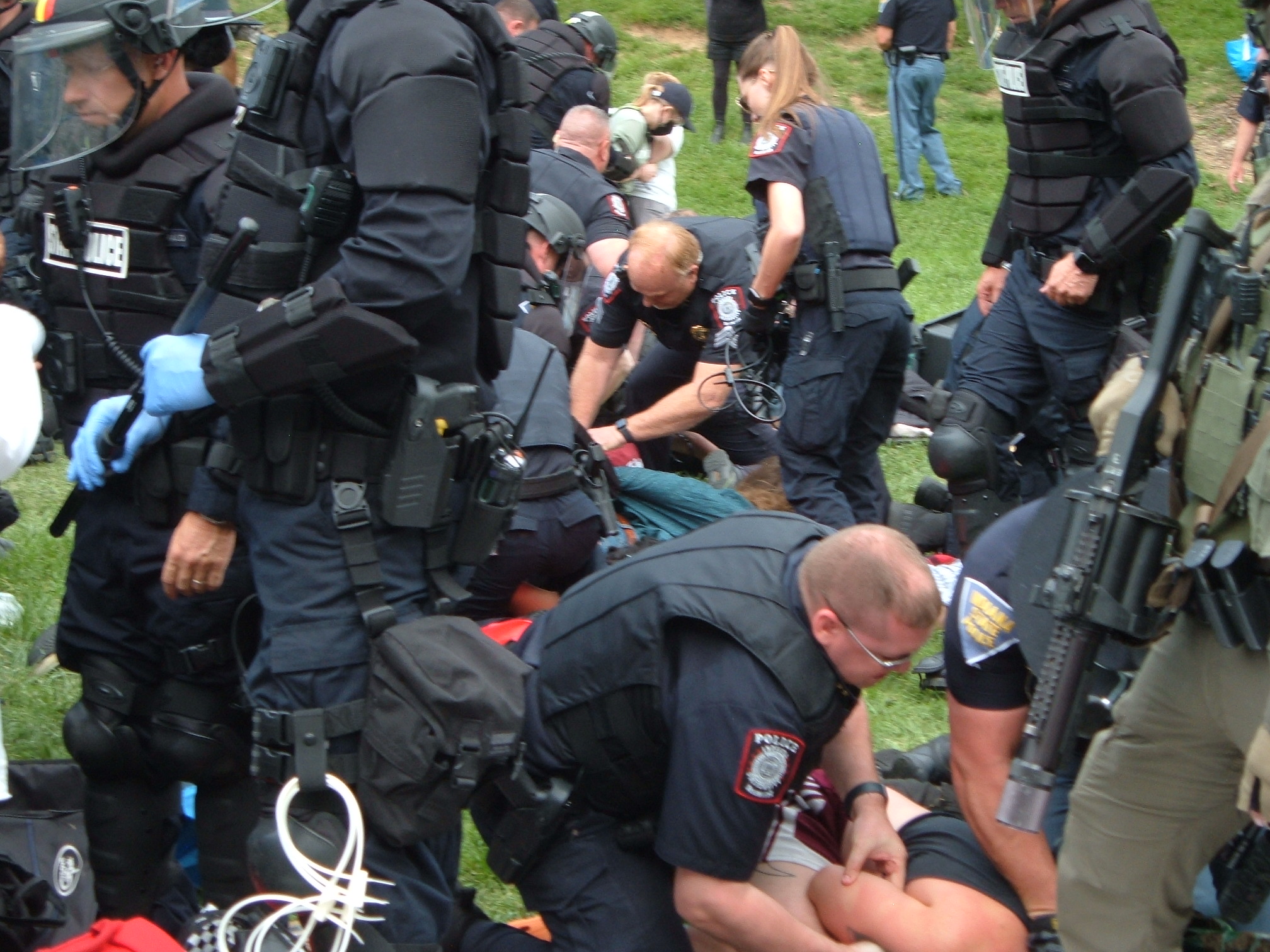 Indiana State Police in riot gear dominate the whole frame as they conduct arrests, a mass of black bullet-proof armor.